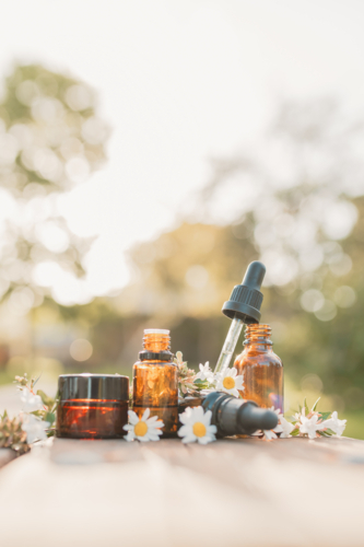 Collection of various amber essential oil bottles in natural outdoor setting with fresh flowers - Australian Stock Image