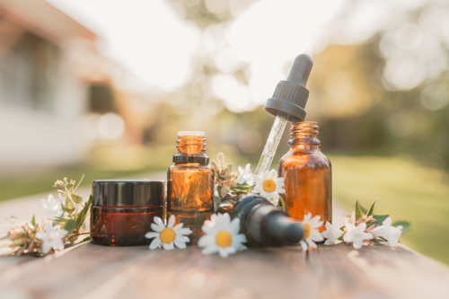 Collection of various amber essential oil bottles in natural outdoor setting with fresh flowers - Australian Stock Image