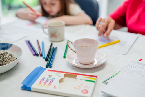 Coloured pencils scattered on a well-lit table with cups of tea - Australian Stock Image