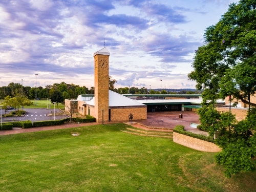 Coloured sky and clouds over green lawn and brick council buildings in town - Australian Stock Image