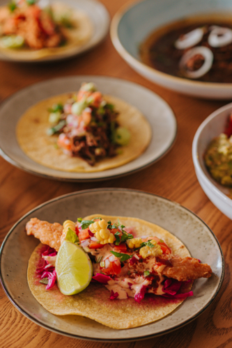 Colourful Fish Taco Served on a Plate With Lime and Garnish Alongside Other Dishes - Australian Stock Image
