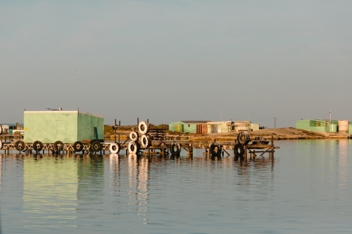Colourful fishing shacks and sheds with wooden jetty and water reflections - Australian Stock Image