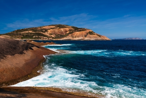 Colourful rocky foreground with dark turquoise water and deep blue sky - Australian Stock Image