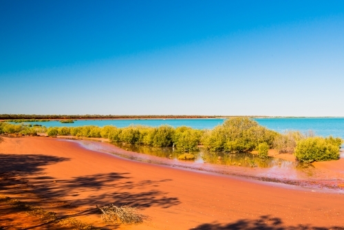 Colourful seascape, with layers of red sands, green mangroves, turquoise water and clear blue sky - Australian Stock Image