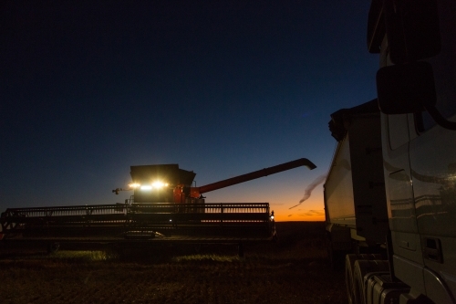 Combine harvester about to unload grain into a semi trailer truck at night - Australian Stock Image