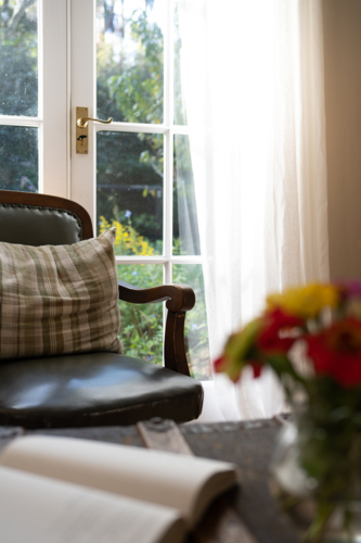 Comfortable chair by window with book and flowers - Australian Stock Image