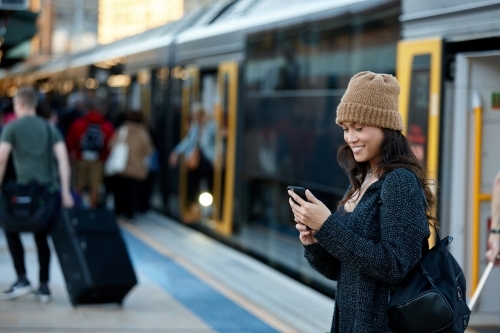 Commuter coming off train at station using mobile phone