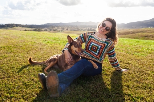 Companions - happy middle age woman and kelpie dog sitting together on farm hilltop - Australian Stock Image