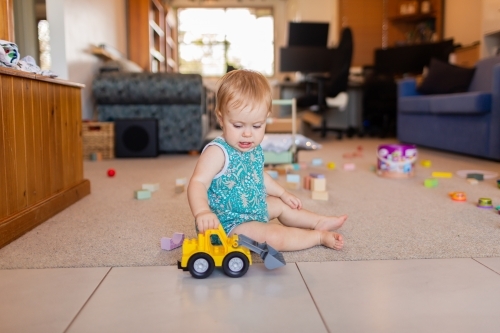 Content baby playing on floor with digger toy in messy lounge room of home - Australian Stock Image