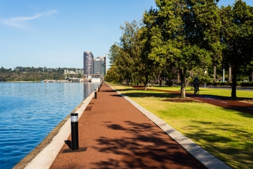 Converging lines of orange path, path lights and trees beside blue water with building and blue sky