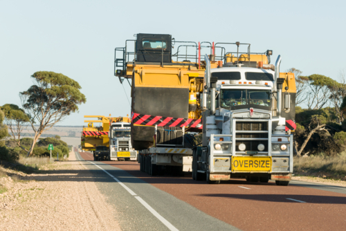 Convoy of trucks transporting oversized mining equipment on an outback highway - Australian Stock Image
