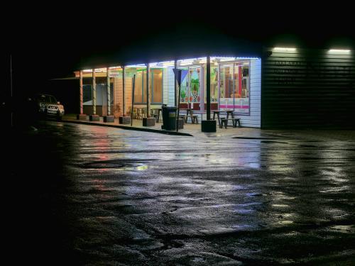 Corner store at night with light reflected on a wet road - Australian Stock Image