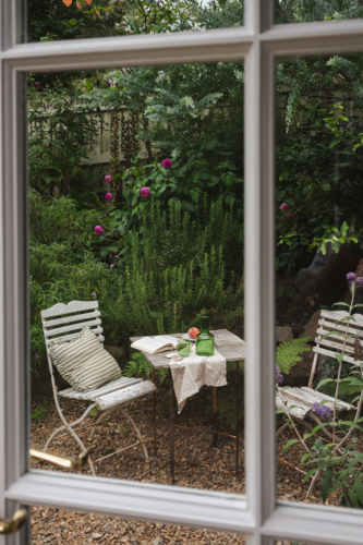 Cosy garden table with two white, weathered metal chairs and flower arrangement - Australian Stock Image