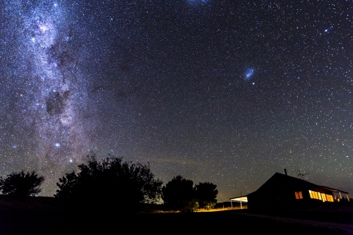Cottage at night with lights in windows and starry sky - Australian Stock Image