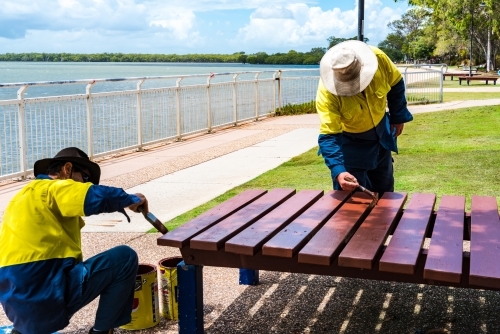 Council workers painting outdoor park benches and tables in Moreton Shire - Australian Stock Image