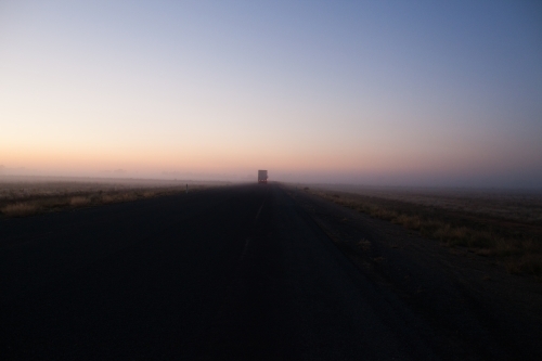 Country highway at sunrise with semi trailer truck driving off in distance