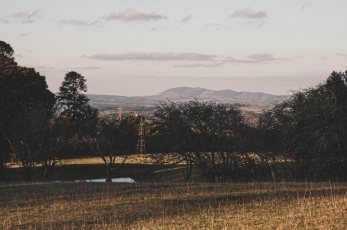 country pasture view at sunset with a windmill and mountains in th background - Australian Stock Image