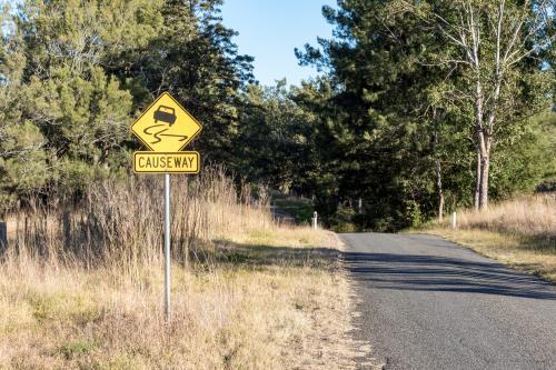 Country road with a causeway warning sign positioned beside the roadway, indicating potential water - Australian Stock Image