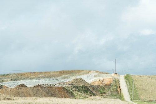 country road leading over a hill past an old quarry in muted tones - Australian Stock Image