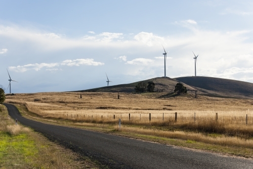 Country road leading through paddocks with wind turbines - Australian Stock Image