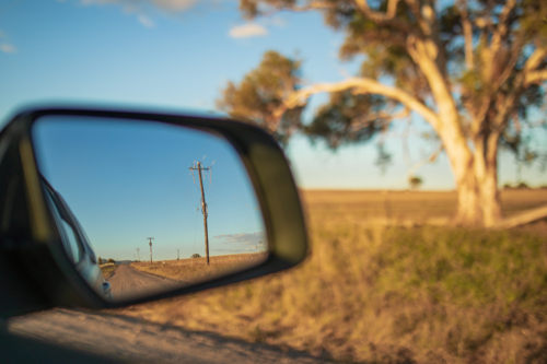 Country road lined with power lines visible in side mirror of car on rural Australian road trip - Australian Stock Image