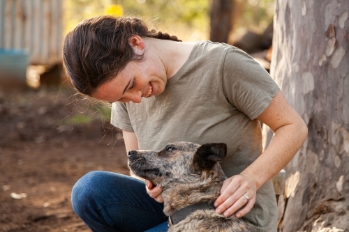 Country woman sitting beside gum tree with pet dog - Australian Stock Image