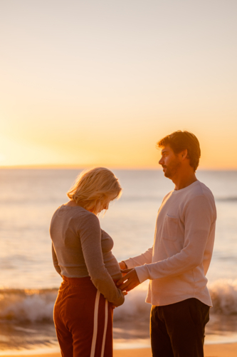 Couple celebrating pregnancy at Manly Beach during sunrise - Australian Stock Image