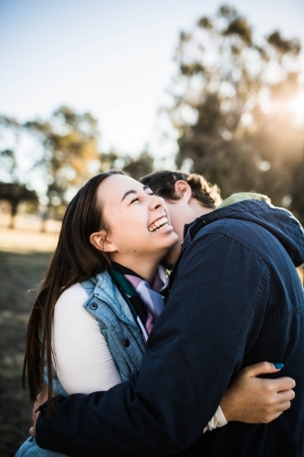 Couple cuddling woman laughing while man kisses her neck - Australian Stock Image