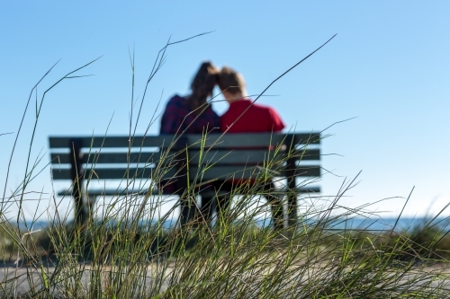 Couple from behind in private moment of park bench - Australian Stock Image