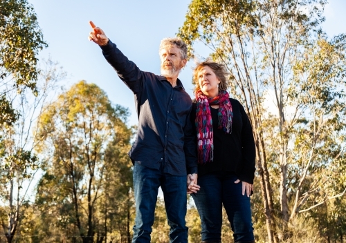 Couple holding hands man pointing into distance - Australian Stock Image