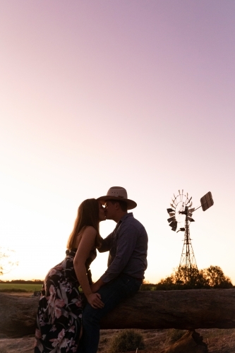 Couple kissing with the man sitting on a log and girl standing in a floral dress - Australian Stock Image