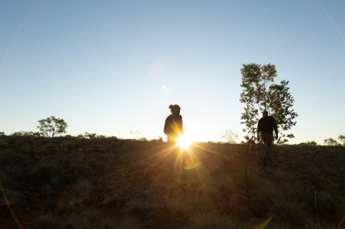 Couple on sunset walk through country paddock landscape - Australian Stock Image