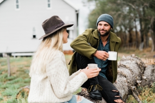 Couple sitting on fallen tree, talking and drinking coffee