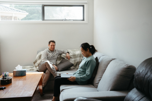 Couple talking while seated on the couch while woman holds a laptop - Australian Stock Image
