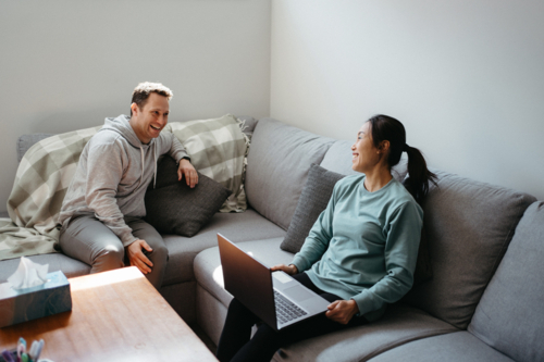 Couple talking while seated on the couch while woman holds a laptop - Australian Stock Image