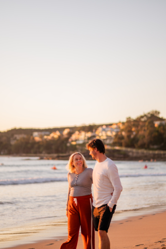 Couple walking along Manly Beach at sunrise - expecting parents - Australian Stock Image