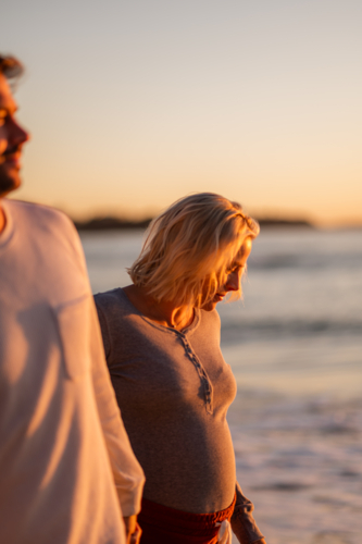 Couple walking hand in hand at Manly Beach during sunrise, celebrating maternity and family - Australian Stock Image