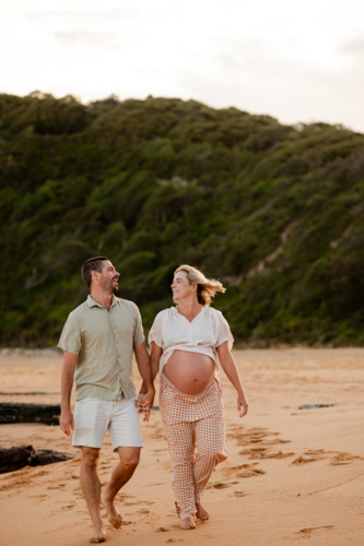 Couple walking hand in hand on the beach during sunset with pregnancy glow - Australian Stock Image