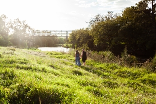 Couple walking on grass at riverside in country - Australian Stock Image