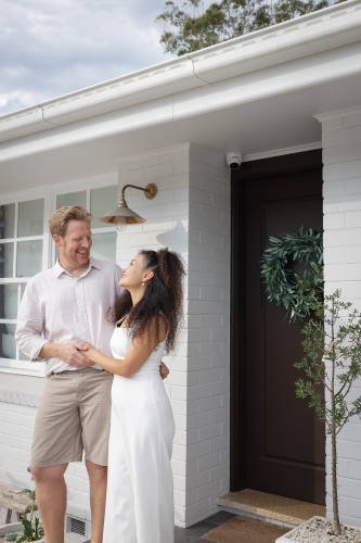 Couple wearing white standing together on front porch - Australian Stock Image