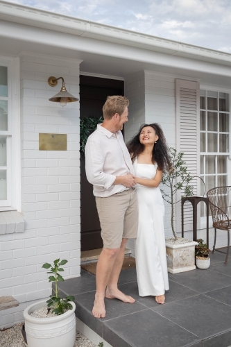 Couple wearing white standing together on front porch - Australian Stock Image