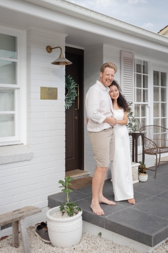 Couple wearing white standing together on front porch - Australian Stock Image