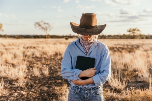 Cowgirl in blue long sleeves holding tablet in paddock - Australian Stock Image