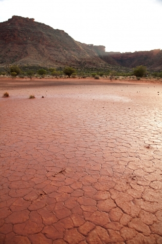Cracked red dry ground with mountains in background - Australian Stock Image