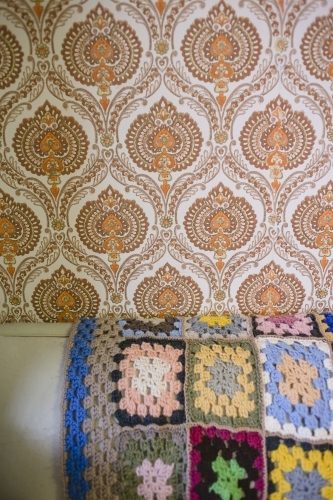 Crochet blanket draped over couch with wallpapered wall - Australian Stock Image