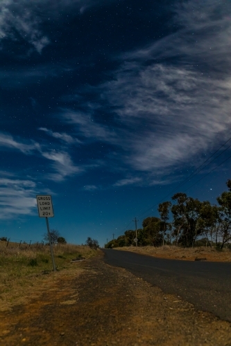 Crooked sign along a country road on a starry partly cloudy night