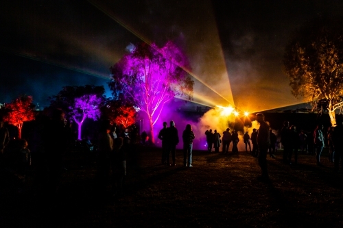 Crowd of people watch night time laser light display beams of colourful light shining on fog