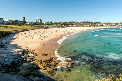 Crowded Bondi Beach on a sunny day with swimmers and sunbathers along the shoreline. - Australian Stock Image
