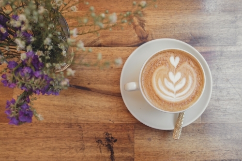 Cup of coffee latte art and flowers on wooden table - Australian Stock Image