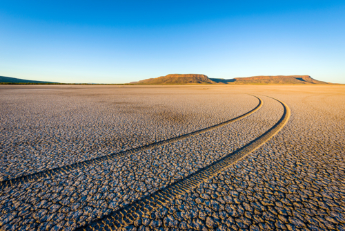 Curving tyre tracks across a dry cracked desert plain at sunrise - Australian Stock Image